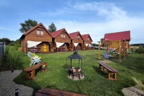 Cabins with balconies and doors with windows are set amidst a well-maintained lawn with a fire pit and seating areas.