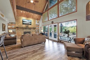 Amplia sala de estar con chimenea, piso de madera y ventanas grandes que ofrecen vistas al exterior.