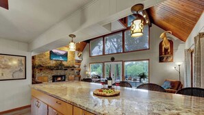 A spacious kitchen with a large island, wooden cabinets, and a stone fireplace.