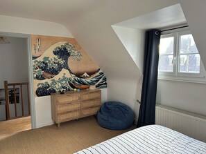 A bedroom with a traditional Japanese wave painting, a wooden dresser, a bean bag, and a window with a view of buildings. - Le Cottage, Jolie Villa à 3 Minutes de la mer ! (Ambleteuse)