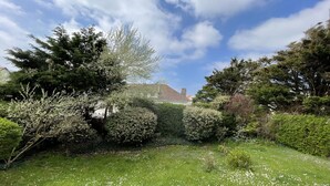 A lush garden with a variety of trees and shrubs, a well-maintained lawn, and a building with a tiled roof in the background. - Le Cottage, Jolie Villa à 3 Minutes de la mer ! (Ambleteuse)