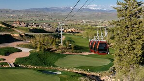 En linbana som färdas över en golfbana med ett bergigt landskap i bakgrunden.