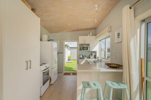 Cocina moderna con armarios blancos, microondas y estufa. Hay dos taburetes y una ventana con cortinas.
