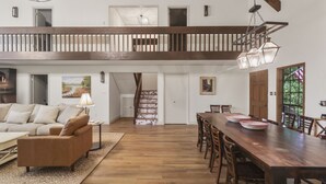 Amplia sala de estar con una mesa de comedor de madera, un sofá y una escalera que lleva a un nivel superior.