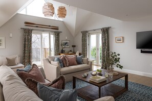 A spacious living room with a high ceiling, large windows, and a flat-screen TV mounted on the wall.