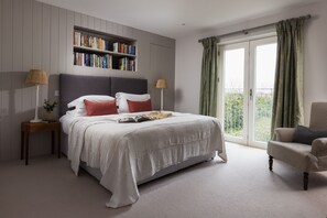 A bedroom with a large bed, a bookshelf, a chair, and a balcony with curtains.