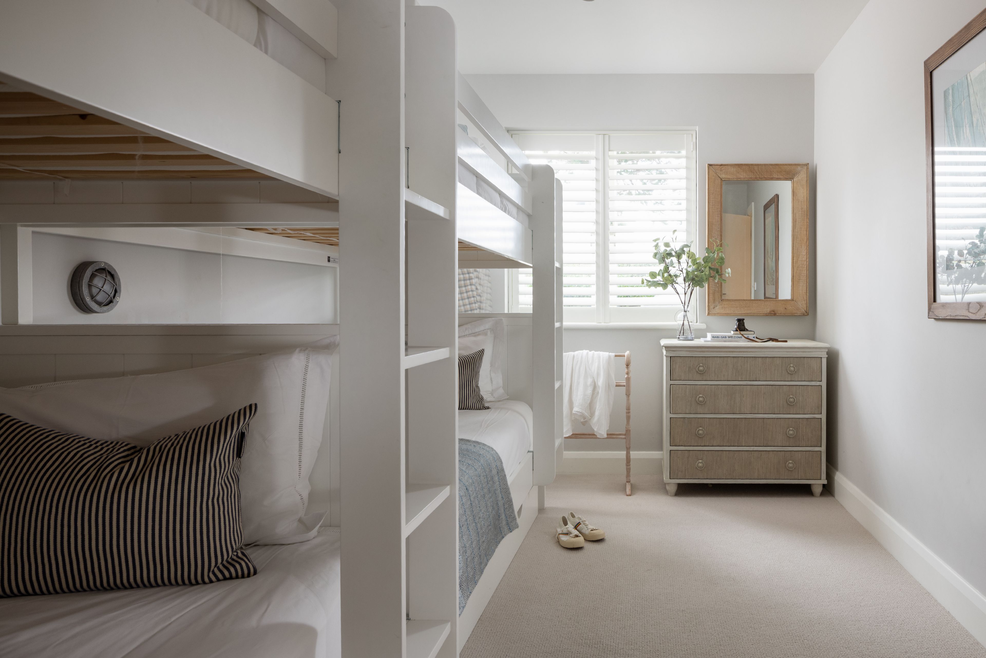 Une chambre avec des lits superposés, une commode, un miroir et une fenêtre avec des stores.