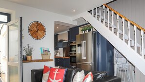 A modern living room with a leather sofa, a wooden clock, and a staircase leading to a kitchen area. - Brigwyn (Pwllheli)