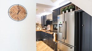 A modern kitchen with dark cabinetry, a stainless steel refrigerator, and a wooden clock on the wall. - Brigwyn (Pwllheli)