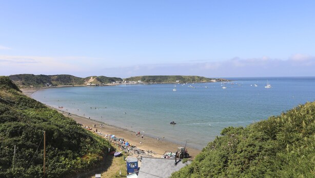 A coastal beach with clear waters, boats, and a hilly landscape. - Brigwyn (Pwllheli)