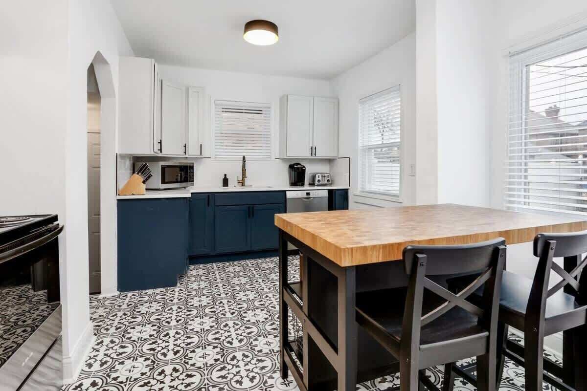 A compact kitchen with white cabinets, a wooden dining table, and black chairs.