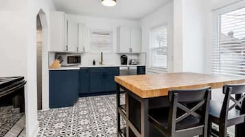 A compact kitchen with white cabinets, a wooden dining table, and black chairs.