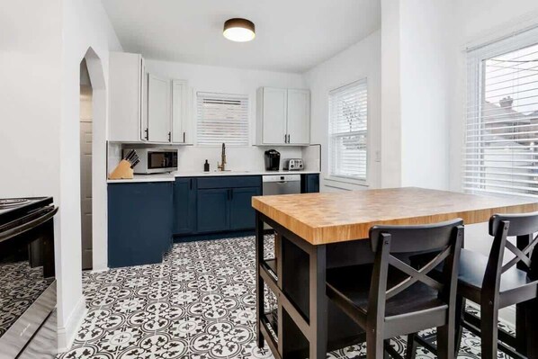 A compact kitchen with white cabinets, a wooden dining table, and black chairs.