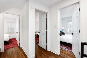 A hallway leading to two bedrooms, each with a bed and a window.
