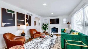 Un salon avec un canapé vert, deux fauteuils en cuir, un tapis à motifs et des œuvres d’art abstraites accrochées au mur.