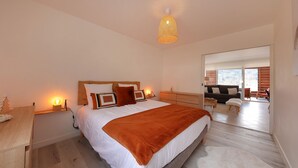A bedroom with a bed, bedside tables, a lamp, and a view of a living area.