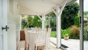 A covered patio with a table and chairs, a white door, and a view of a garden. - Le Gîte de Beauport - Proche des plages (Paimpol)
