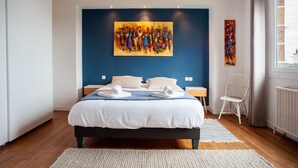 A modern hotel room with a large bed, a blue accent wall, and artwork. - Le Gîte de Beauport - Proche des plages (Paimpol)