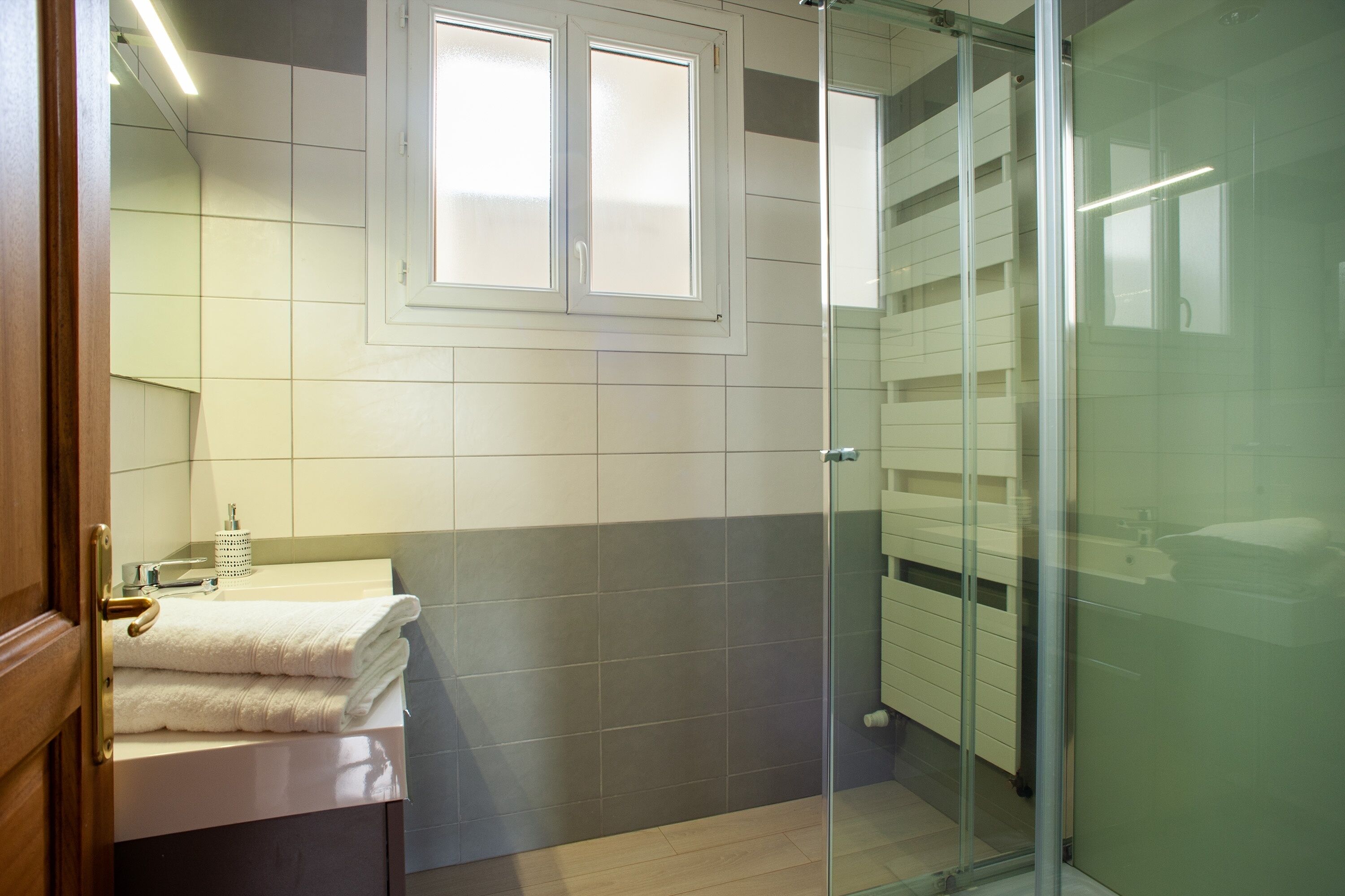 A modern bathroom with a glass shower enclosure, a sink with a mirror, and a window above the mirror.