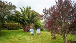 A grassy outdoor area with two striped lounge chairs and a palm tree. - Le Gîte de Beauport - Proche des plages (Paimpol)