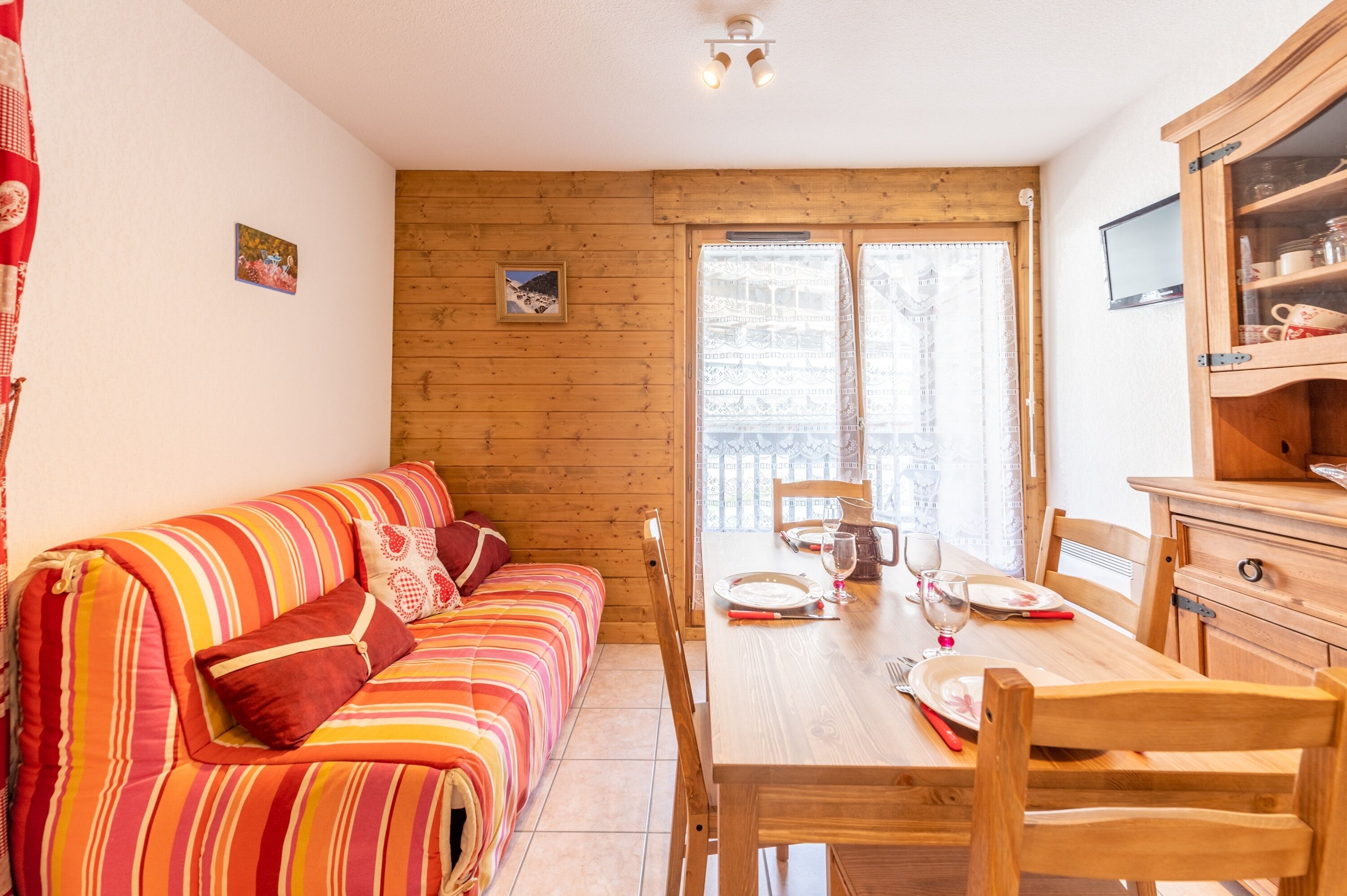 A cozy room with a wooden floor, a striped sofa, a dining table set with plates, glasses, and a chair.