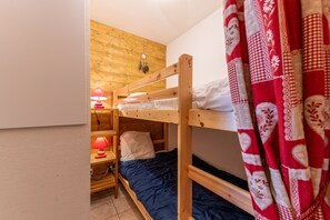 Une chambre avec un lit superposé, un mur en bois, un rideau à motifs rouges et blancs, et une petite table avec une lampe rouge.