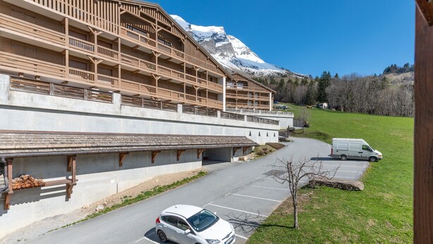 A building with multiple balconies, a parking area, and a snow-capped mountain in the background.