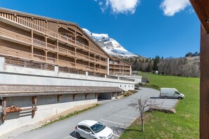 Ein Gebäude mit mehreren Balkonen, einem Parkplatz und einem schneebedeckten Berg im Hintergrund.
