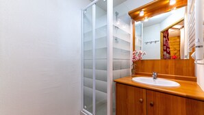 A bathroom with a glass shower enclosure, a wooden vanity with a sink, and a mirror with lights above.