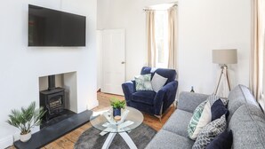 Un salon moderne avec une cheminée, un fauteuil bleu, un canapé gris, une table basse en verre et un lampadaire.