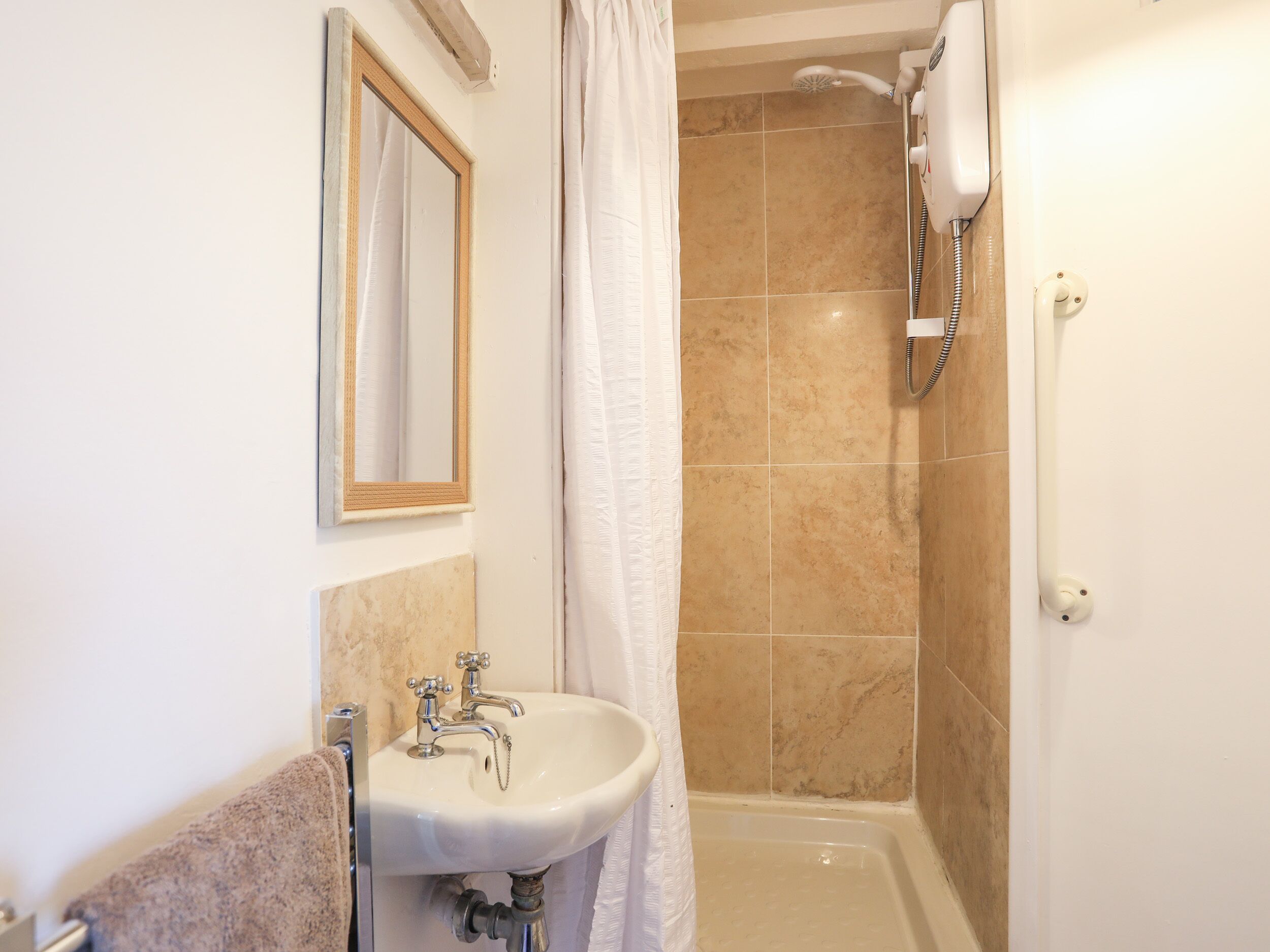 A bathroom with a sink, mirror, shower, and a telephone.