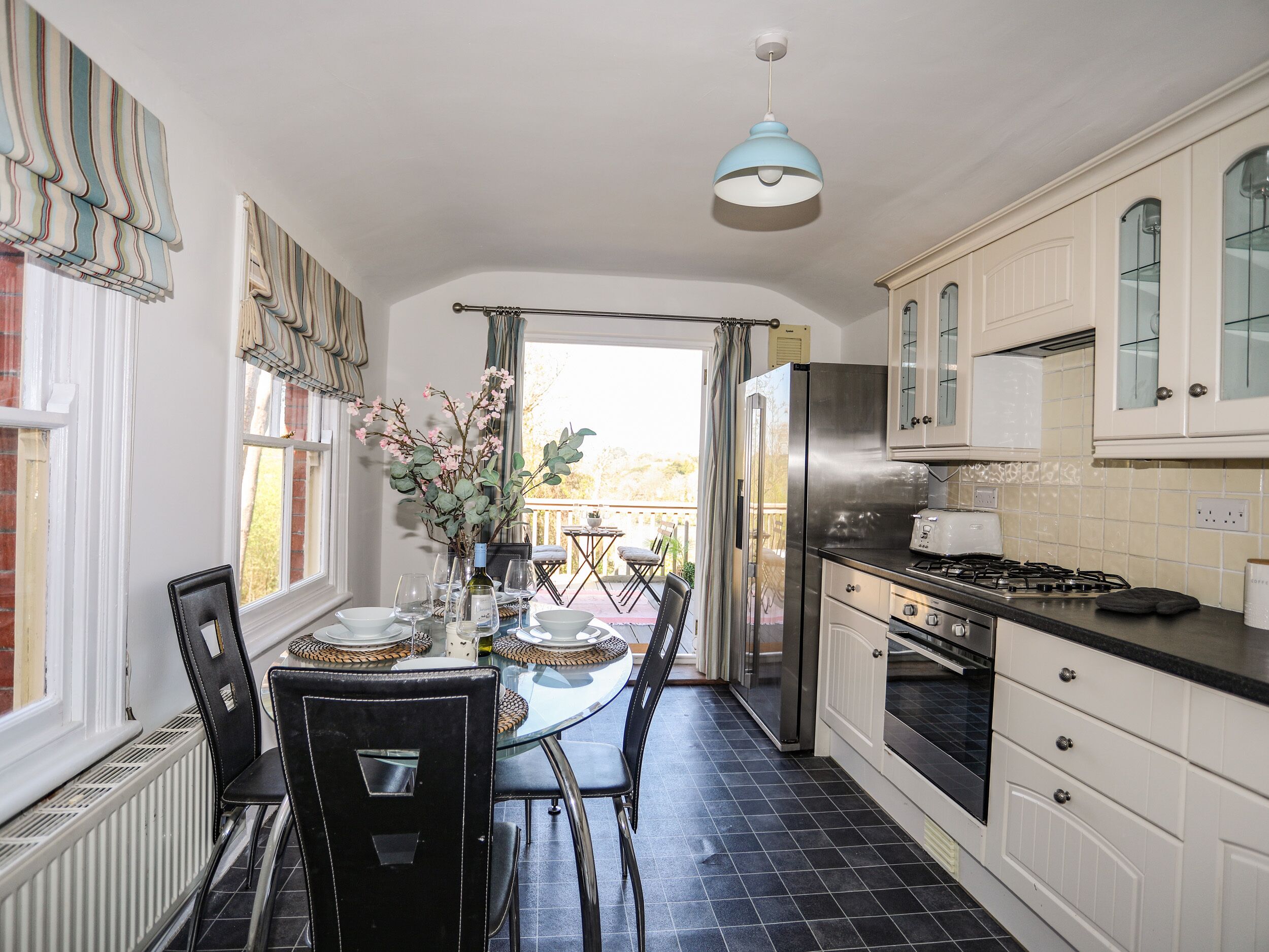 A kitchen with a dining area, featuring a table set for four, a refrigerator, a stove, and a view to the outside.