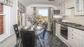 Une cuisine avec coin repas, comprenant une grande fenêtre, un réfrigérateur, un four et une table à manger pour six personnes.