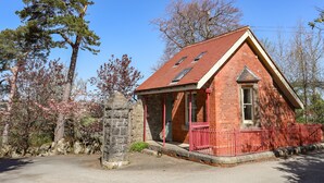 Un petit bâtiment en briques avec un toit rouge, un pilier en pierre et une clôture rouge.