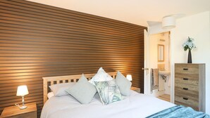 Une chambre à coucher avec une tête de lit en lattes de bois, un lit avec plusieurs oreillers, une table de chevet avec une lampe et une commode avec des tiroirs.