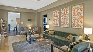 A living room with a green sofa, two patterned armchairs, a coffee table, and a bookshelf.