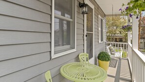 A porch with a green metal table and chairs, a hanging flower pot, and a white railing.