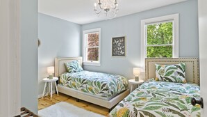 A bedroom with two beds, a chandelier, and a view of trees through the window.