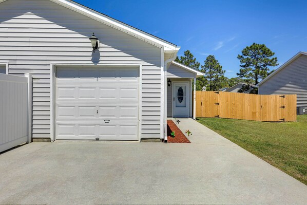 A single-story house with a white garage door, a front porch with a small step, and a wooden fence in the backyard.