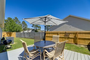 A backyard with a deck, a round table with chairs, a grill, and a wooden fence.