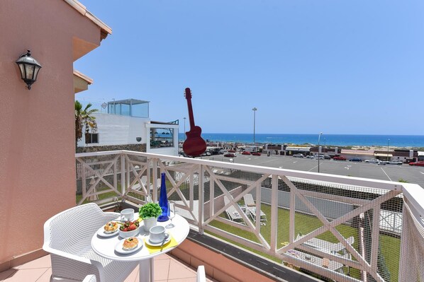 Un balcón con una mesa para dos, con vistas a un estacionamiento y al mar.