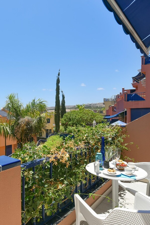 Un balcone con tavolo apparecchiato per mangiare, affacciato su un giardino e edifici.