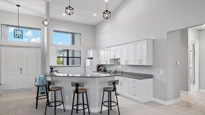 Une cuisine moderne avec des meubles blancs, un plan de travail en granit et trois tabourets de bar.