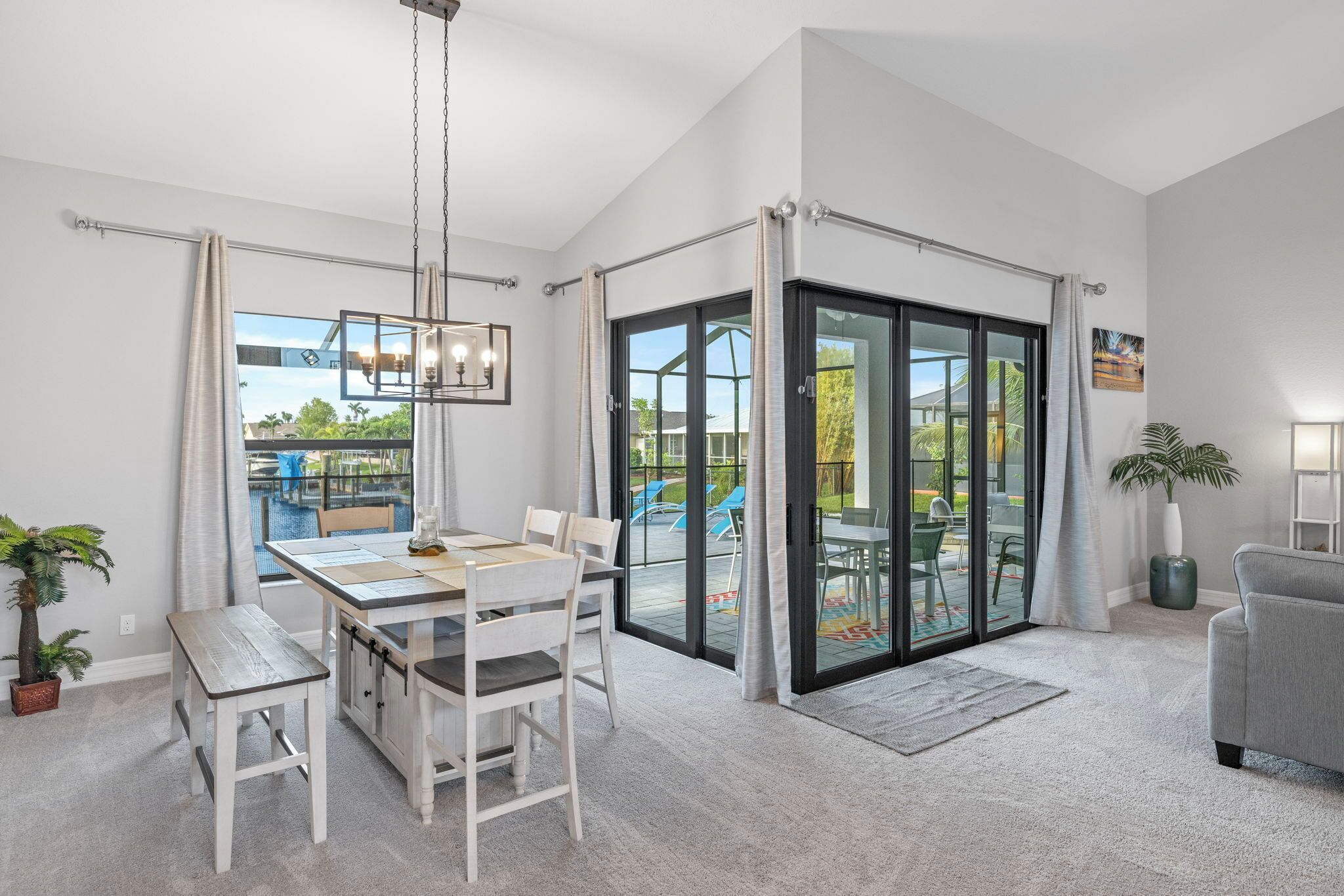 Una sala moderna con comedor, puertas correderas de cristal amplias hacia un patio exterior y un sofá gris.