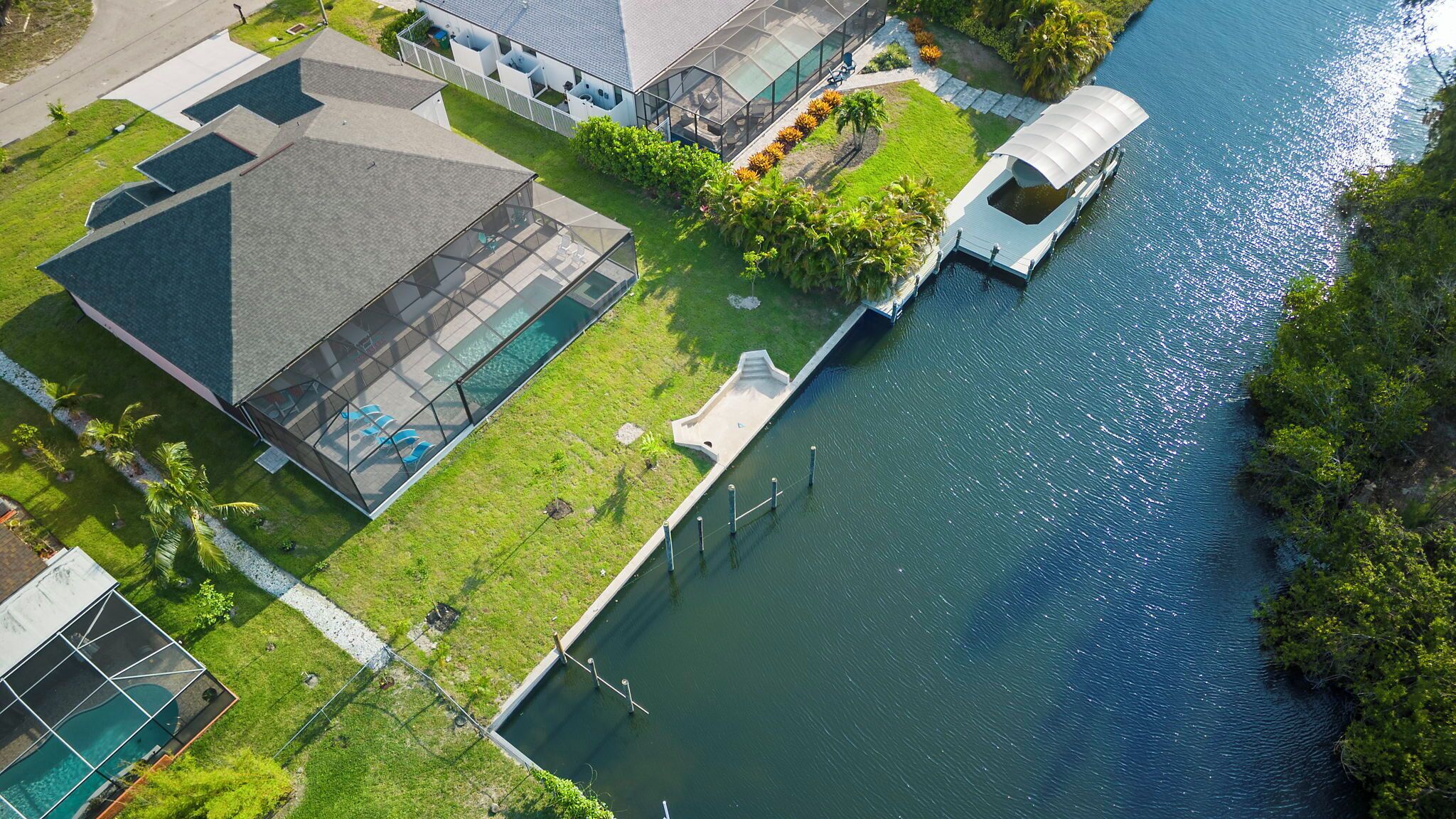 Vista aerea di una proprietà sul lungomare con piscina, un molo coperto per barche e un giardino curato.