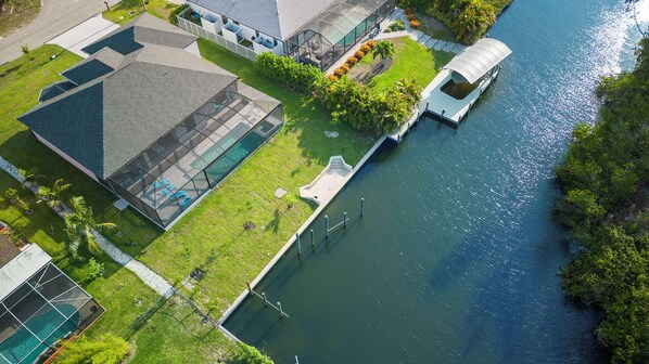 An aerial view of a waterfront property with a swimming pool, a covered boat dock, and a landscaped garden.