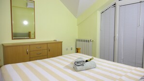 A bedroom with a bed, a wooden dresser, a radiator, and a window with blinds.