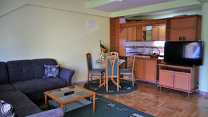 Una sala de estar con sofá, una mesa de centro y un comedor con sillas y una mesa. Hay una cocina con armarios de madera y un televisor.