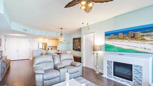 A spacious living room with a grey leather sofa, a fireplace, and a large painting of a beach scene. - New Listing P5-0906 2B Portofino Island View! (Pensacola Beach)