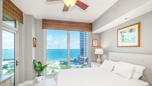 A bedroom with a large bed, a ceiling fan, a view of the ocean, and a window with a view of a tall building. - New Listing P5-0906 2B Portofino Island View! (Pensacola Beach)